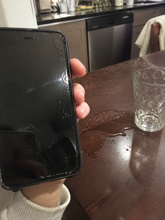 Wet phone on a kitchen counter next to a spilled glass of water